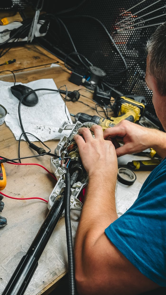Technician repairing an electronic device with tools on a workbench in a workshop setting.